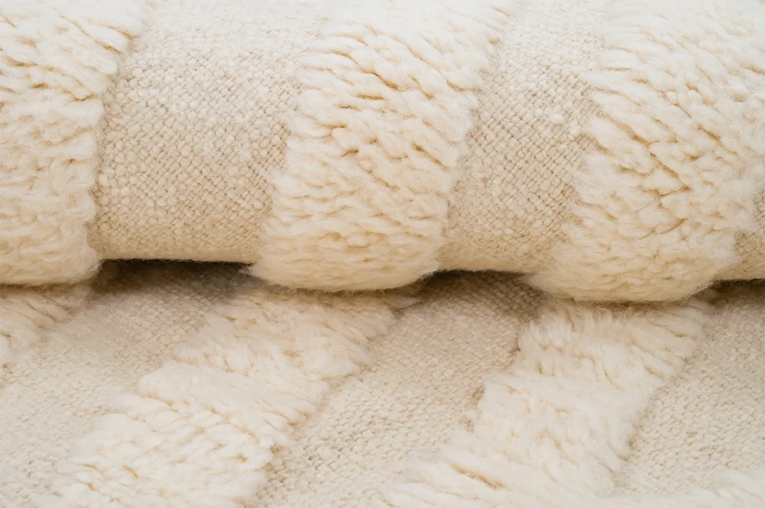 Close-up view of a rolled, cream-colored, textured rug with alternating smooth and fluffy striped patterns.