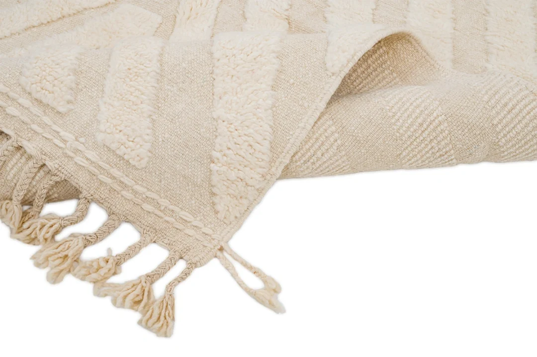 A close-up of a beige textured woven rug with fringed edges on a white background.