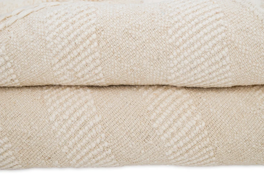 Two folded cream-colored textured rug with a subtle diamond pattern stacked on top of each other.