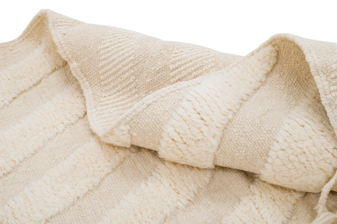 A close-up view of a folded, cream-colored textured rug with alternating smooth and fluffy striped patterns.