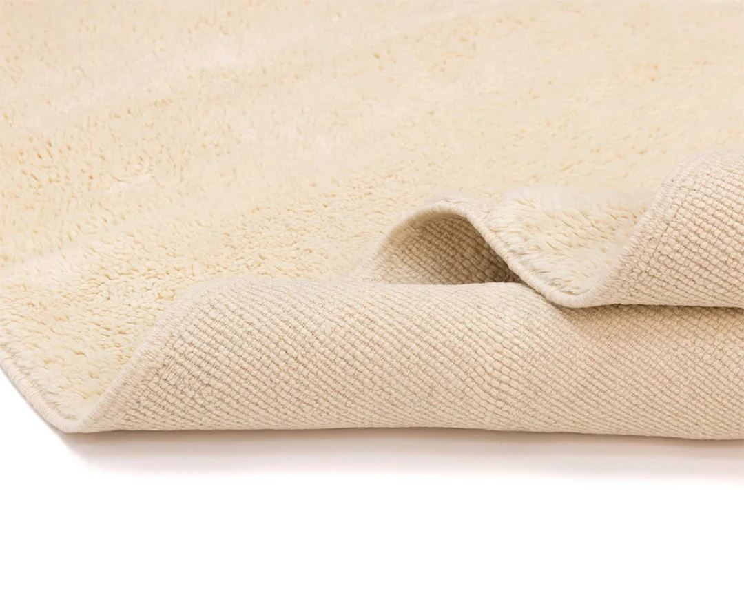A close-up view of a beige, textured, rectangular rug with one corner partially folded over, showing the underside.