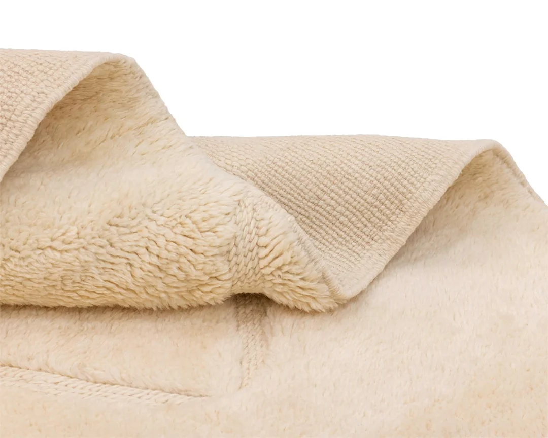 Close-up of a beige, soft-textured fleece blanket folded over itself, showing both the fluffy and smooth sides.