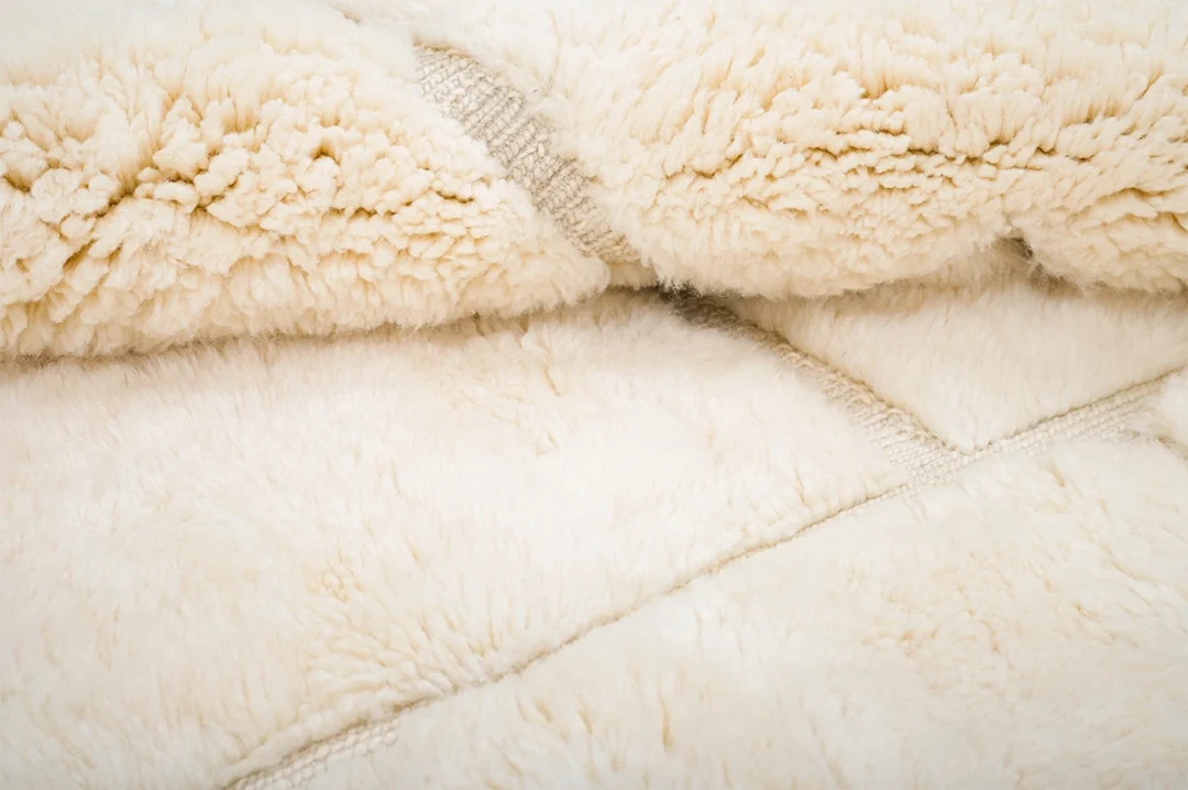 Close-up view of a soft, cream-colored wool rug showing its fluffy texture and fabric seams.