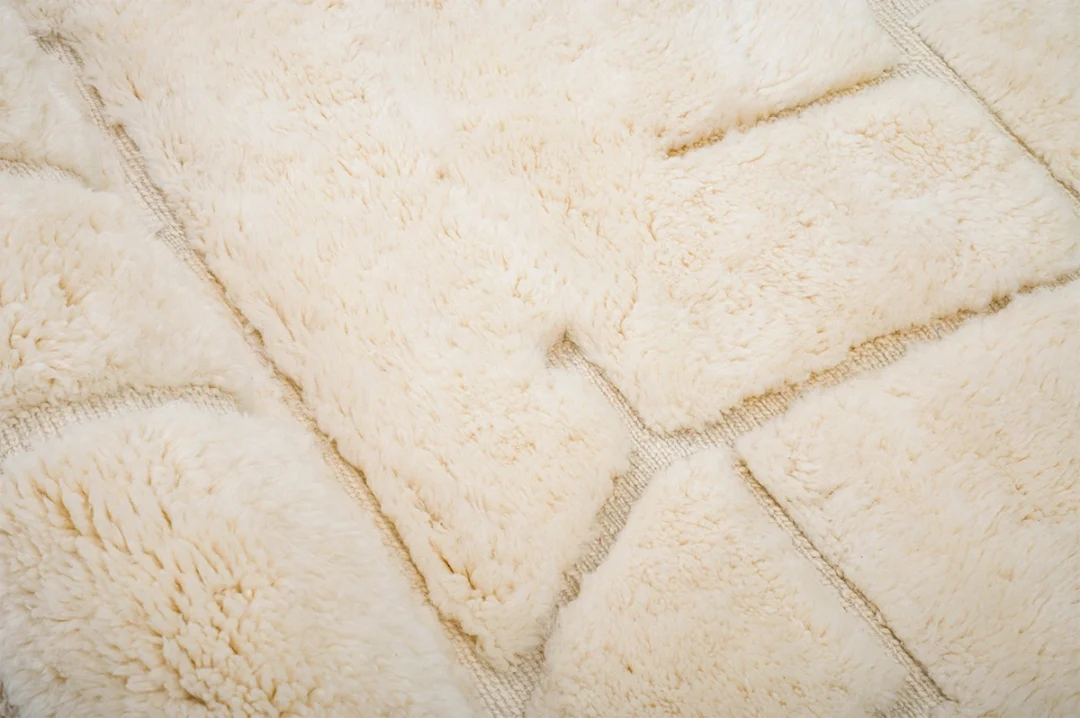 Close-up of a soft, cream-colored, textured rug with rectangular and irregular shaped sections.