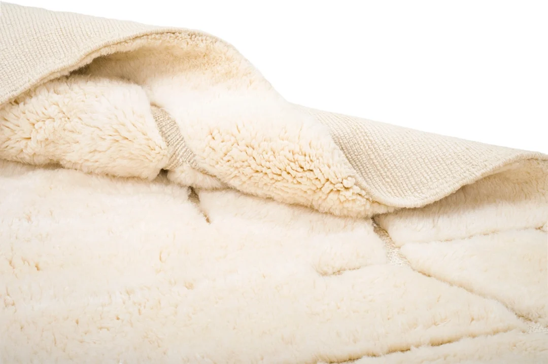 Close-up of a cream-colored, fluffy rug with a textured backing partially folded over, revealing the soft, plush surface and underside material.