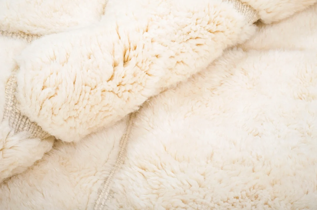 Close-up of a soft, off-white, fluffy wool rug with visible texture and decorative lines.