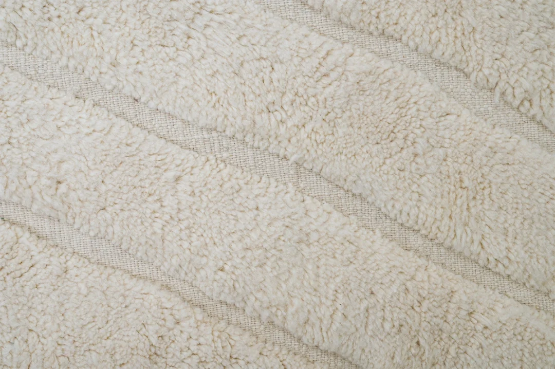 Close-up of a textured, cream-colored, faux fur fabric with diagonal ridges running across the surface.