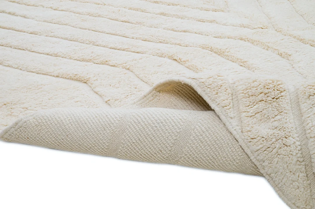 A close-up of a beige, textured rug with one corner flipped over, showing the woven underside.