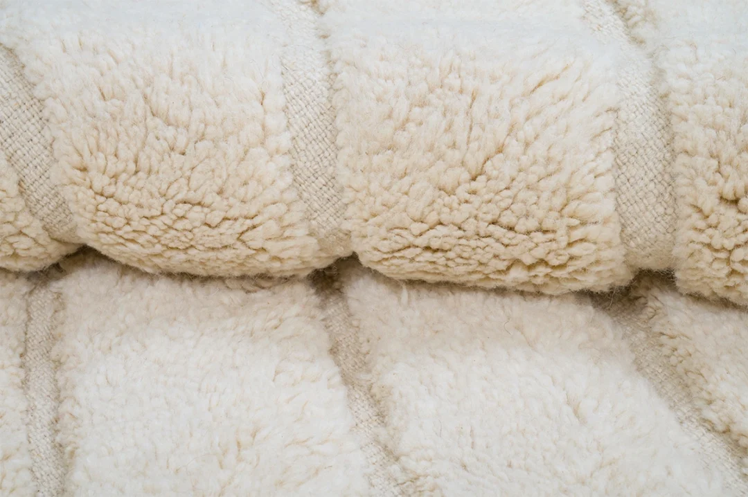 Close-up of a folded, cream-colored, fluffy textured fabric, possibly a blanket or towel, with visible woven lines.