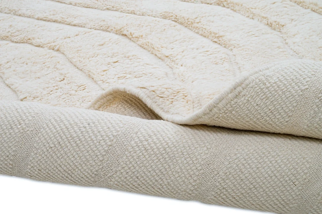 A close-up view of a beige textured rug, partially folded to show its soft, plush surface on top and a woven underside.