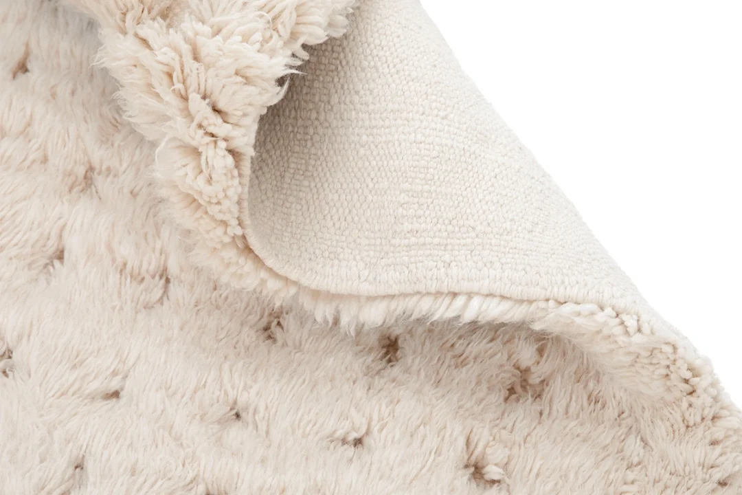 Close-up of a cream-colored, textured rug with the corner folded over to show the woven underside and the soft, fluffy surface.