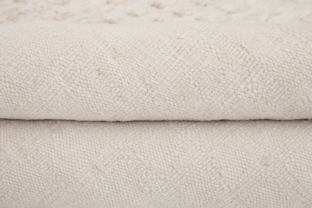 Close-up view of a folded, textured beige rug with a subtle woven pattern.