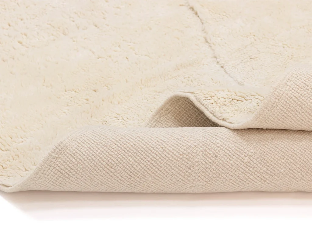 A close-up of a cream-colored, textured rug showing both the soft, plush top surface and the woven underside.