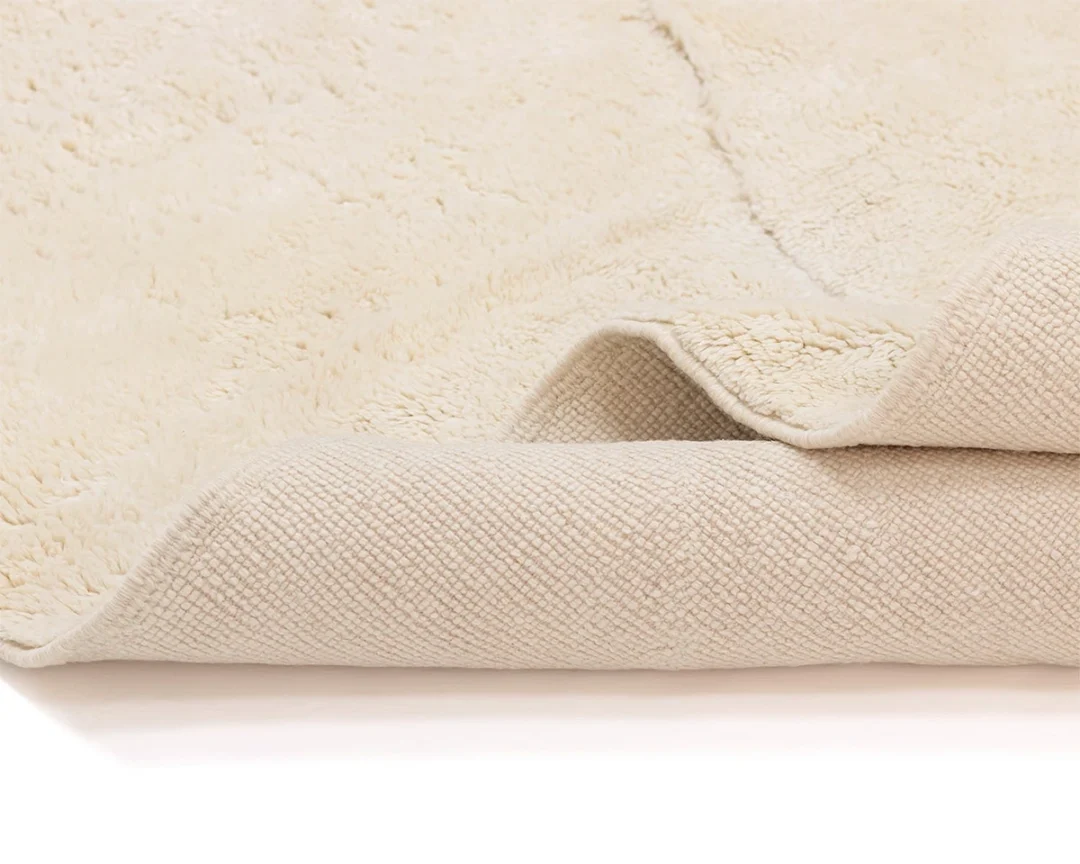 A close-up of a cream-colored, textured rug showing both the soft, plush top surface and the woven underside.