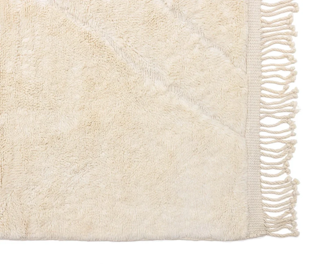 Close-up of a beige textured rug with diagonal lines and fringed edges on one side.