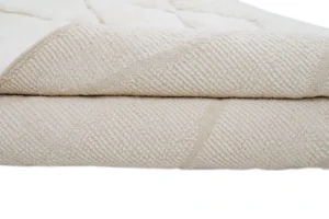A close-up view of a thick, folded, cream-colored textured blanket or rug with a subtle geometric pattern.