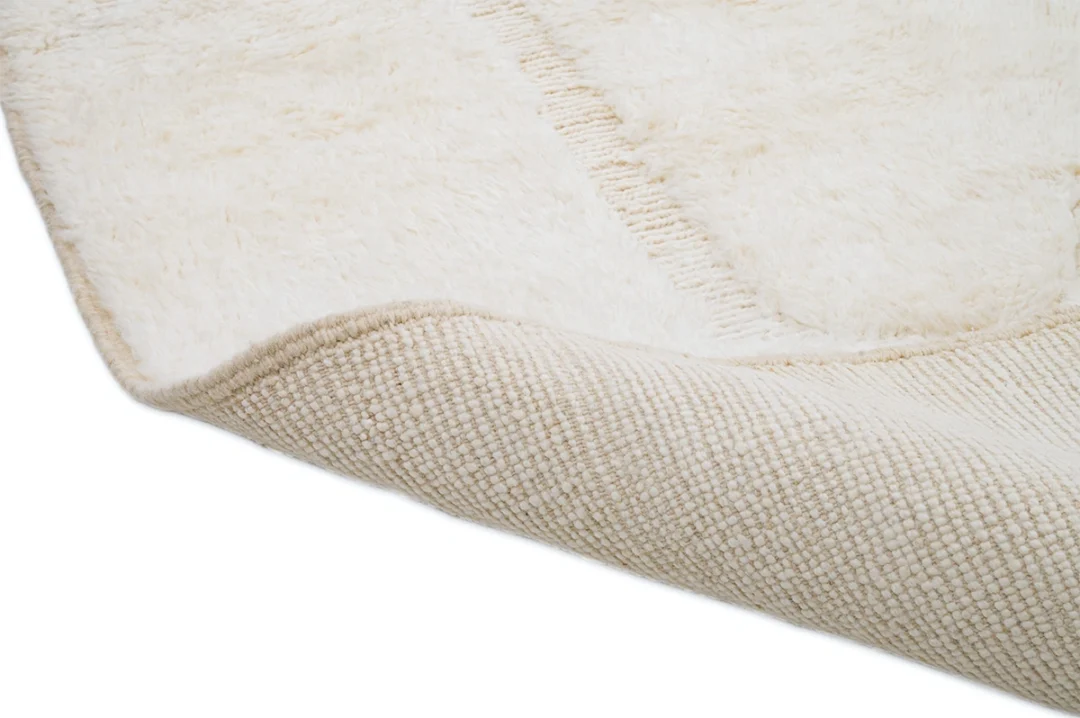 Close-up of a cream-colored textured rug, partially folded to show the soft, plush surface on top and the woven backing underneath.