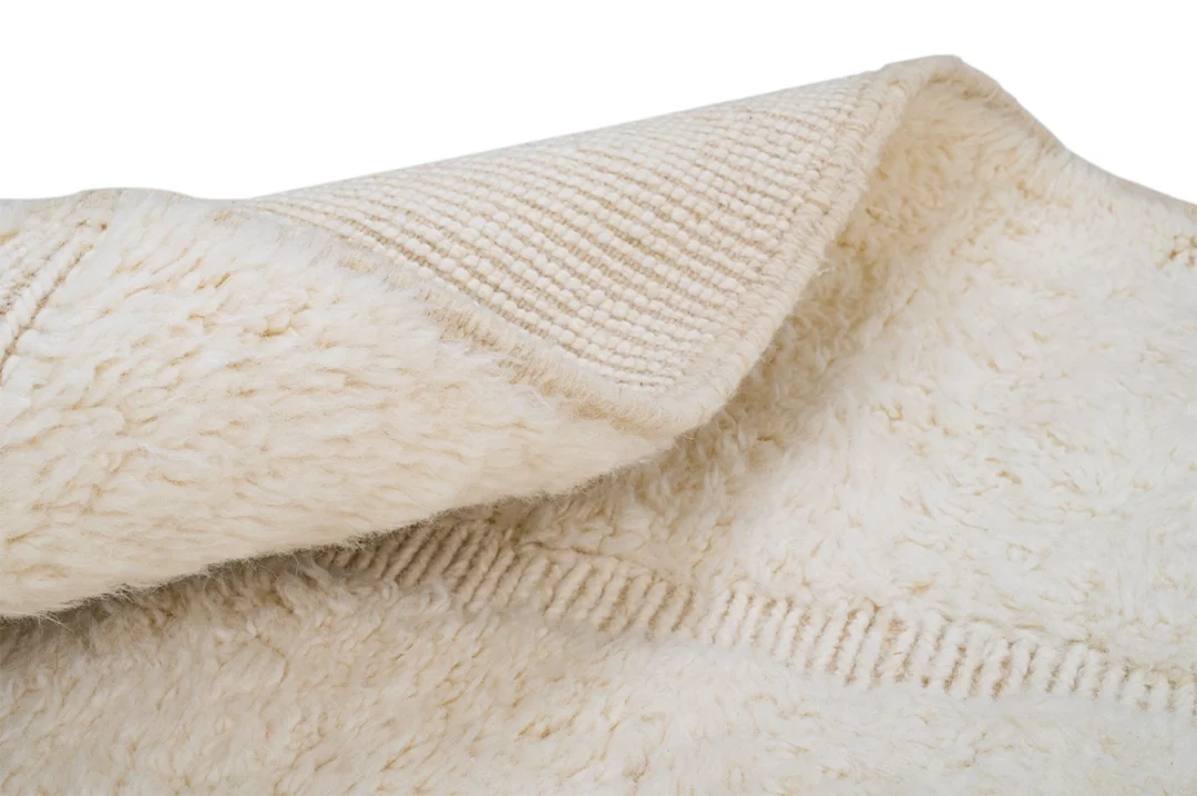 Close-up of a cream-colored, textured blanket or rug with one corner folded over, showing both the soft, fluffy side and the woven underside.