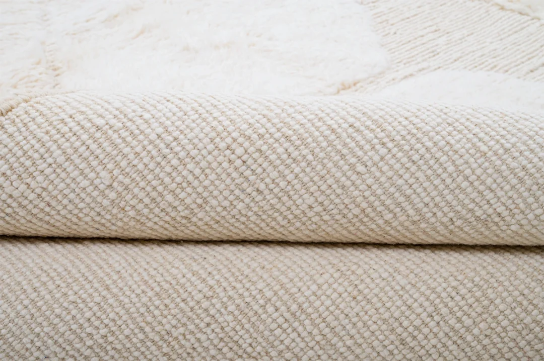 A close-up view of a folded, cream-colored textured fabric or blanket with a woven pattern.