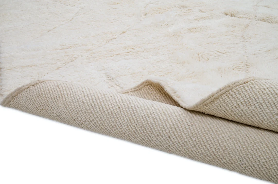 A close-up of a cream-colored rug, partially folded to show both the soft, textured top surface and the woven underside.