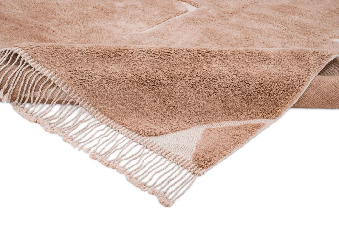 A close-up of a beige, fringed blanket with a soft, plush texture, showing detail of the corner and the tasseled edge.