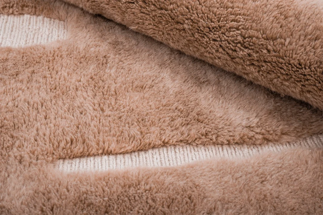 A close-up view of a beige, fluffy, textured carpet partially rolled to reveal its underside.