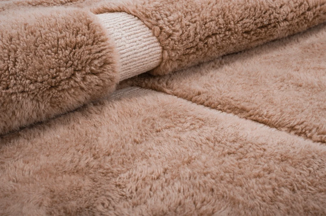 Close-up of a beige, fluffy, faux fur fabric roll partially unrolled, showing the soft texture and the woven backing.