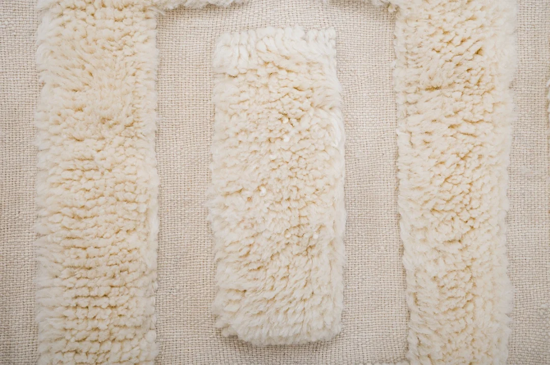 Close-up of textured cream-colored fabric, with a rectangular shaggy section bordered by similar shaggy strips on a coarse woven background.