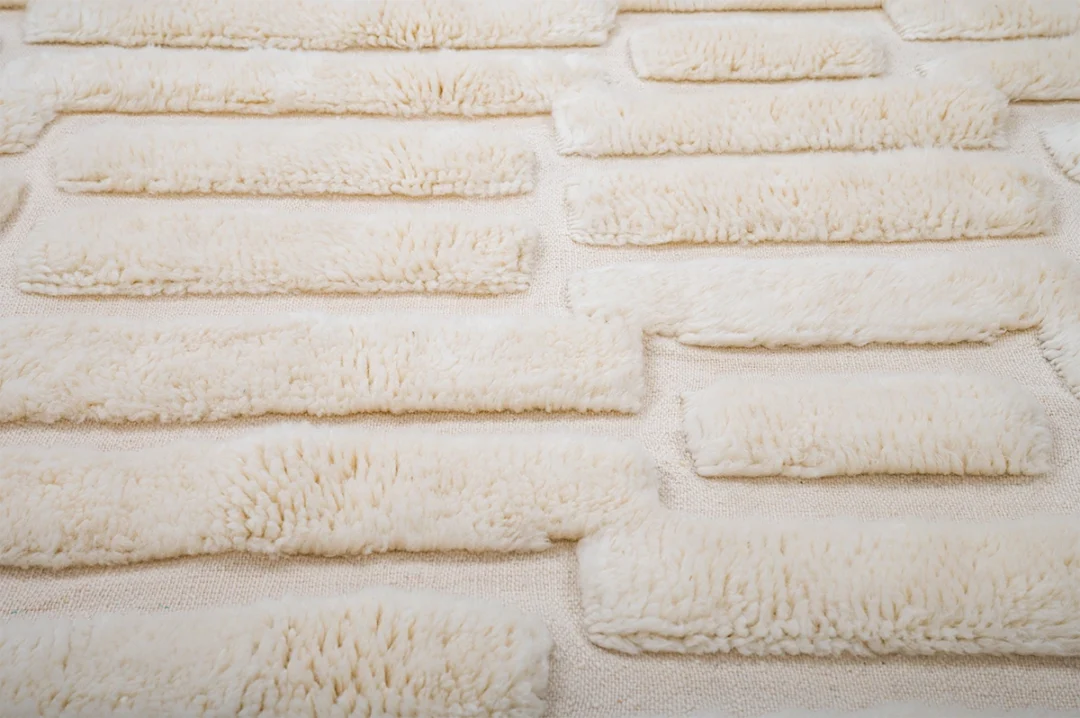 Rows of rectangular, cream-colored, fluffy fabric pieces arranged in a grid pattern on a matching textured surface.