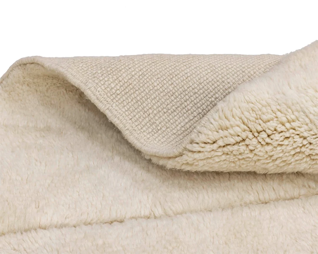 A close-up of a beige fleece rug showing its soft, fluffy side and textured, woven underside.
