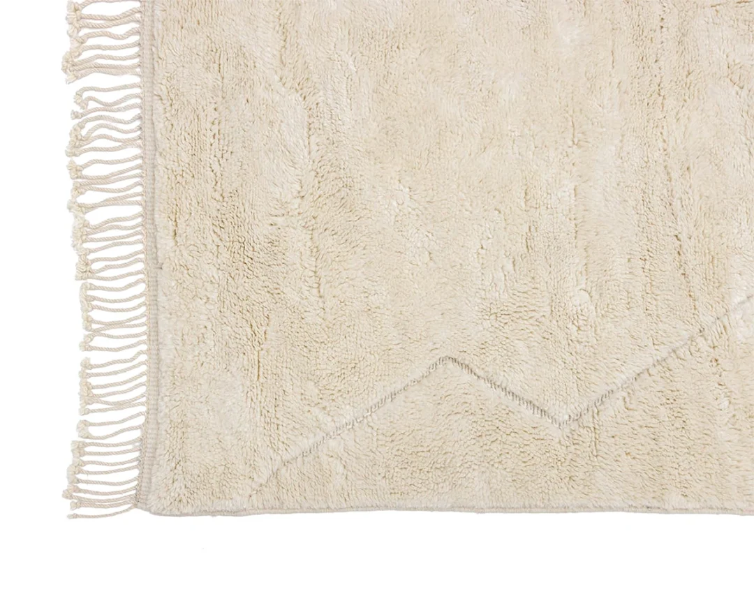 A close-up of a beige, textured rug with a zigzag pattern and fringe detail along one edge.