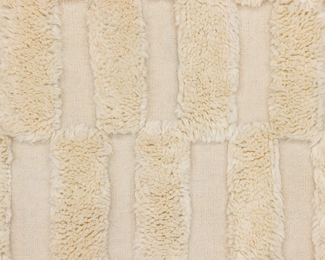 Close-up of a beige textile with alternating rows of shaggy, textured fabric strips and flat woven material arranged in a grid pattern.
