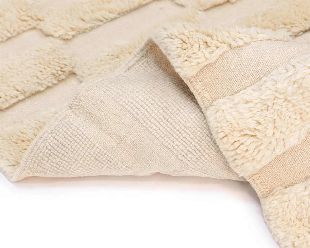 Close-up of a beige, textured rug with a soft, fluffy surface and a woven underside partially folded to show both sides.