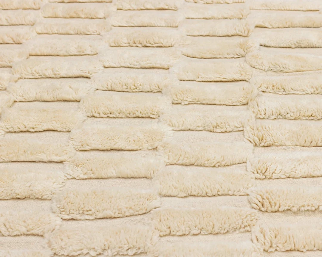 Close-up view of a cream-colored, textured surface with evenly spaced rectangular patches of soft, fluffy material arranged in rows.