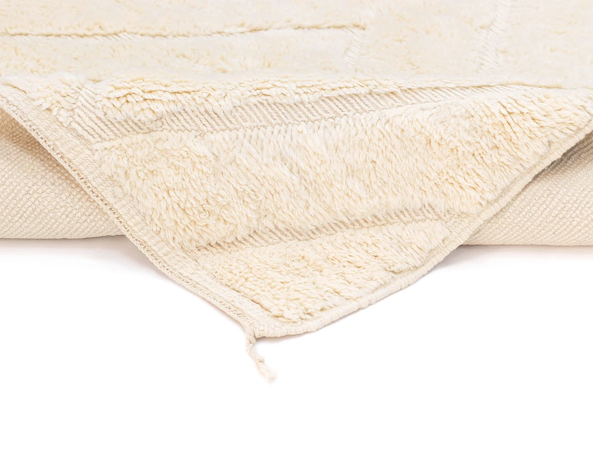 A close-up of a cream-colored textured rug with a corner folded over, showing its soft, plush surface and woven underside.
