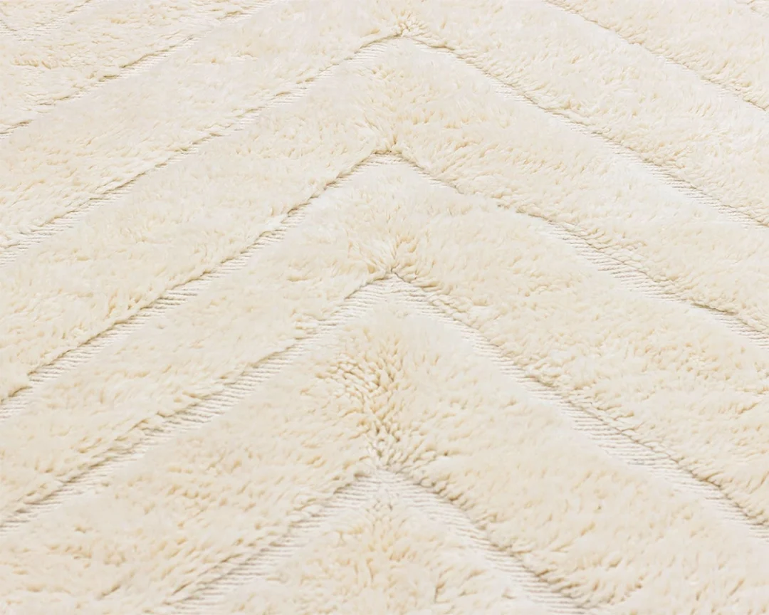 Close-up of a cream-colored, textured rug with a chevron pattern, showing soft, plush material and diagonal lines.