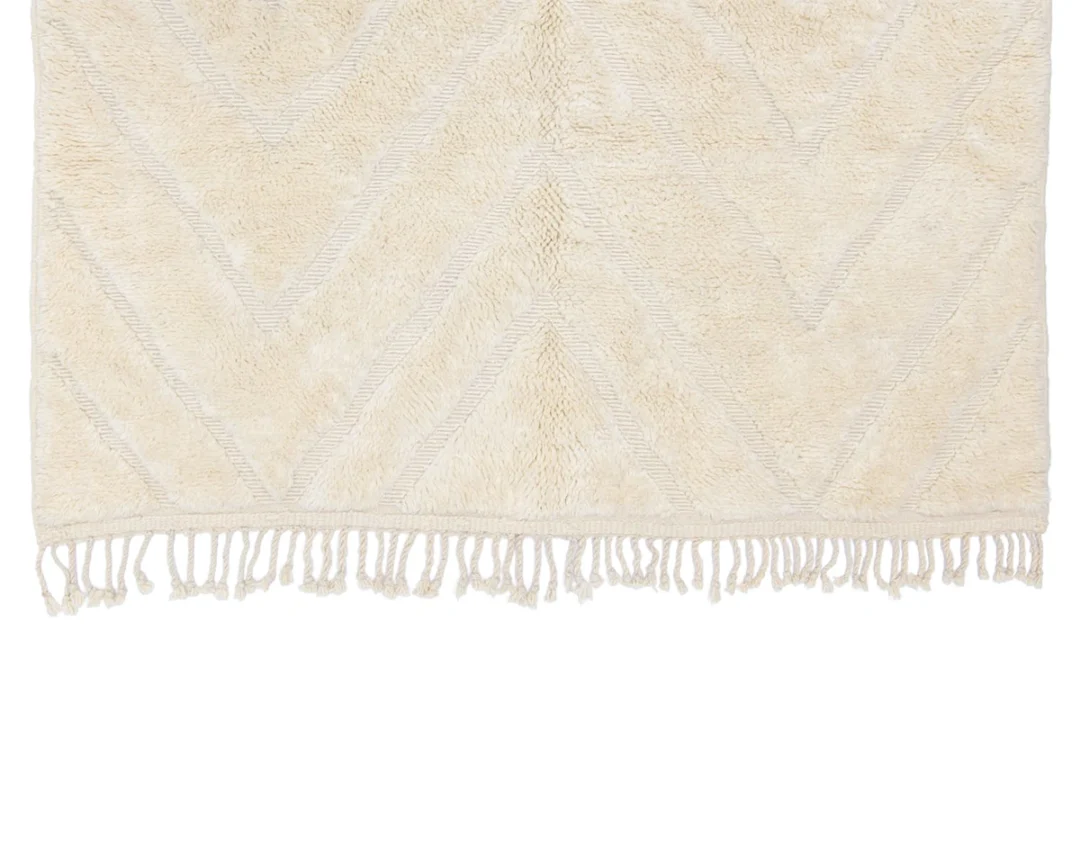 A beige textured rug with a subtle chevron pattern and fringe along the edge.