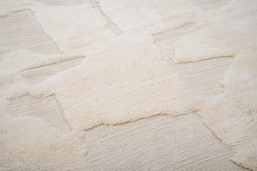 Close-up of a textured cream-colored rug with sections of high-pile and low-pile patterns arranged in geometric shapes.
