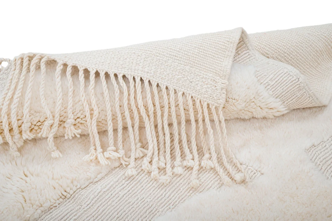 Close-up of a cream-colored woven rug with a fringed edge and a soft, textured surface.