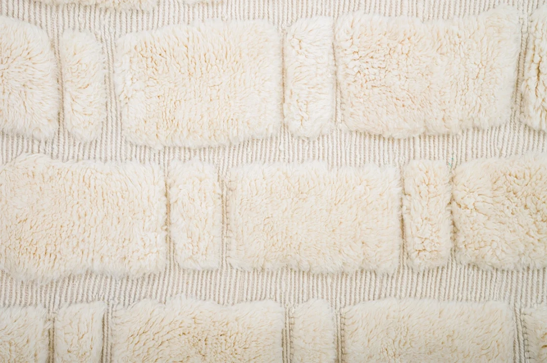 Cream-colored textured rectangles made of soft, fluffy wool are arranged on a ribbed rug background.