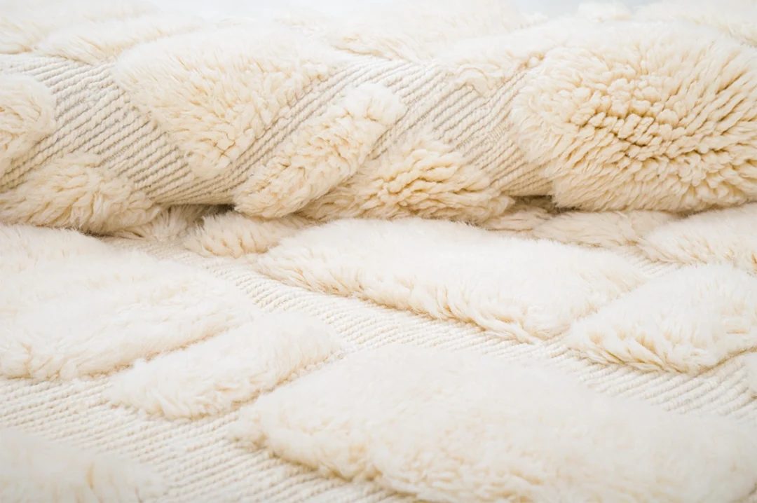Close-up of a cream-colored, textured rug with a geometric diamond pattern and raised, fluffy sections.