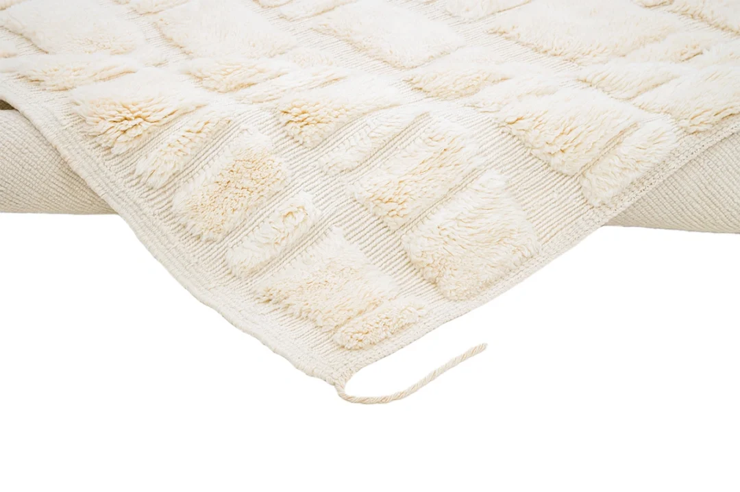 A cream-colored textured rug with raised rectangular patches and a loose yarn strand, displayed against a white background.