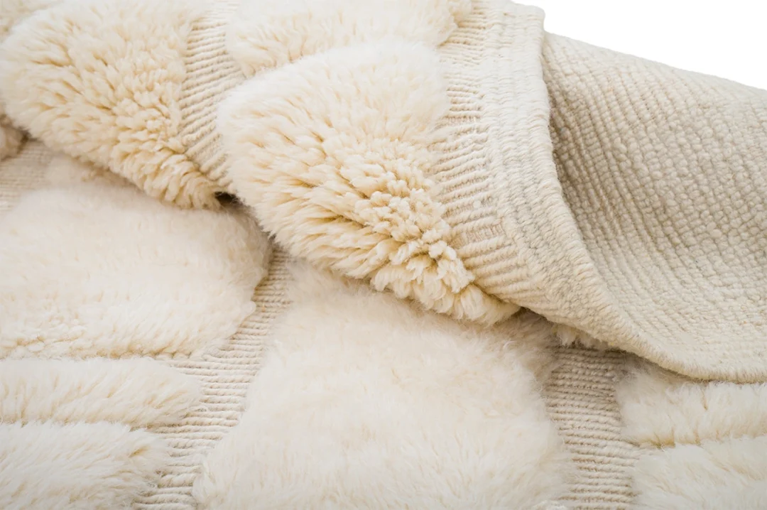 A close-up view of a cream-colored, textured rug showing thick, fluffy piles and a woven base.