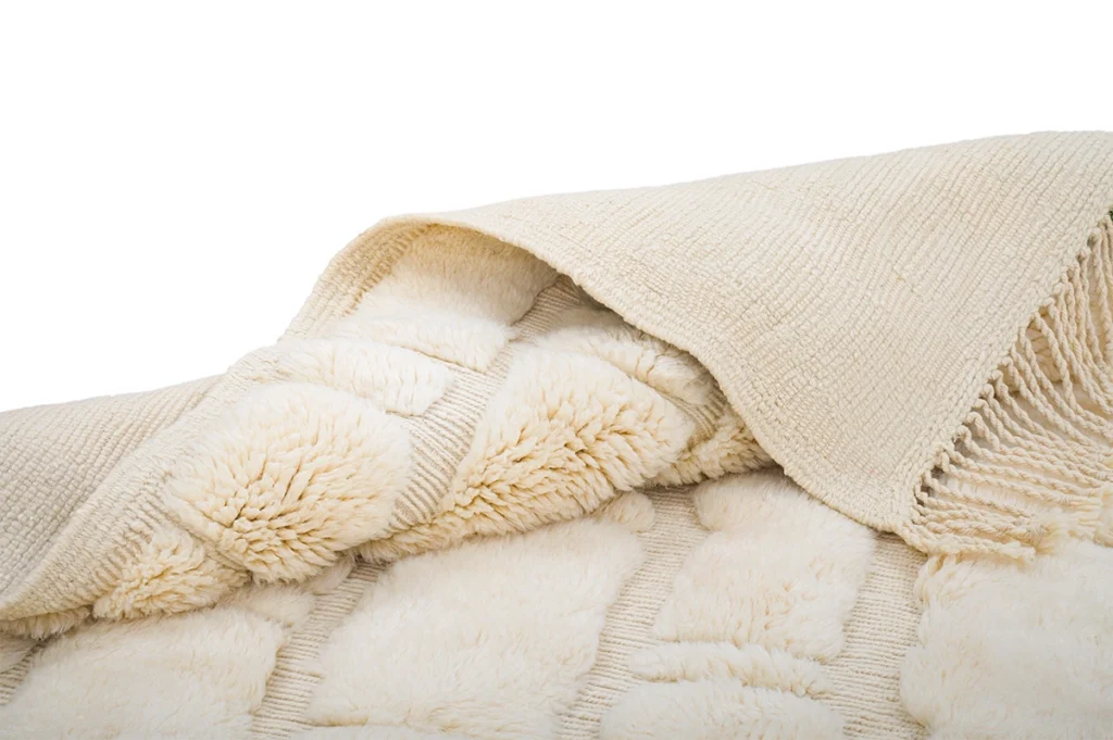 A close-up of a cream-colored textured rug, partially folded to show both its plush and woven sides.