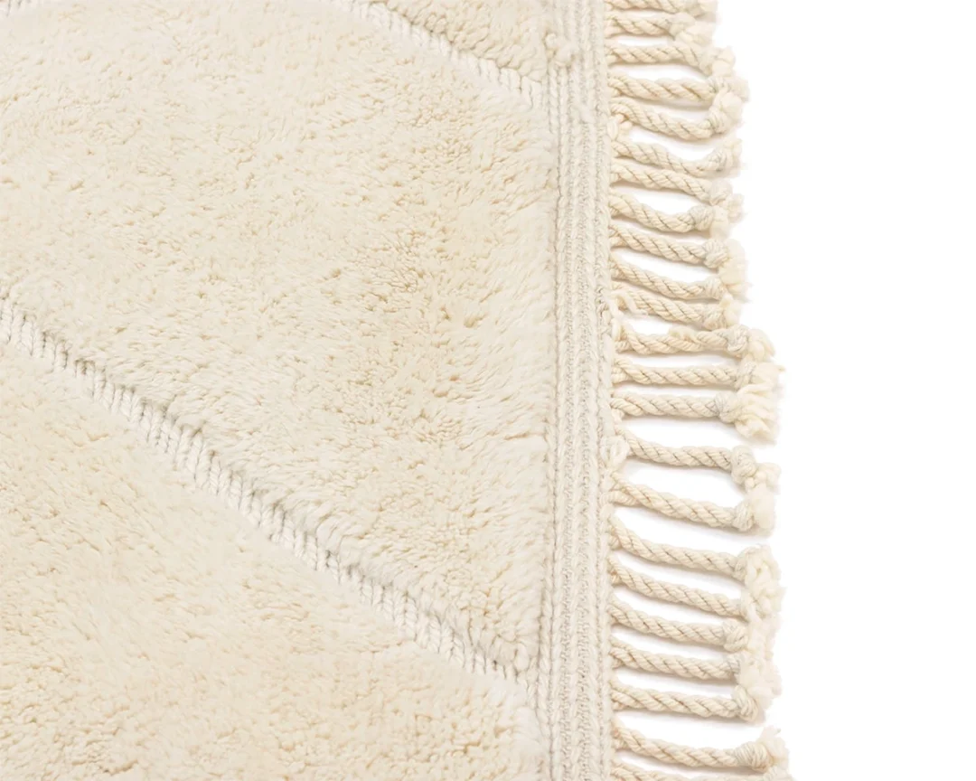 Close-up of a cream-colored textured rug with diagonal lines and twisted fringe tassels along the edge.