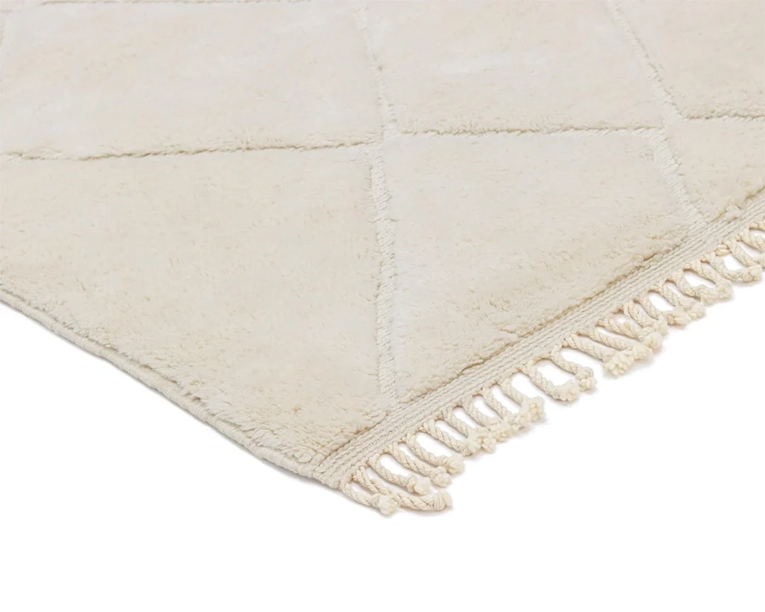 A close-up of a cream-colored rug with a subtle geometric pattern and short fringe on the edge.