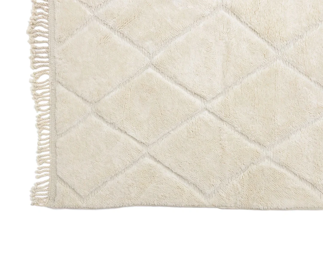 A close-up of a cream-colored rug with a diamond pattern and tasseled fringe on one edge.