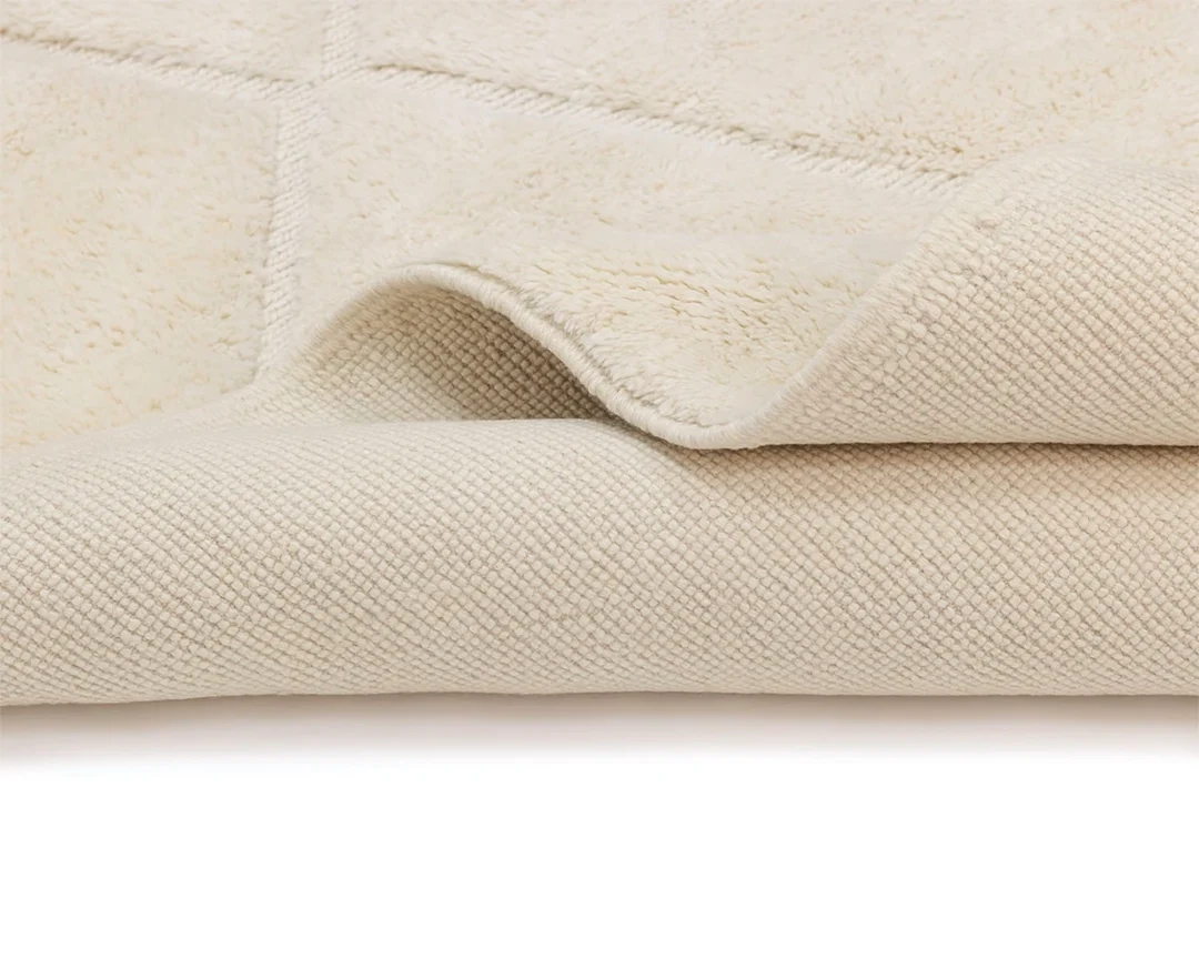 Close-up of a cream-colored textured rug with one corner slightly folded to show both the top and bottom surfaces.