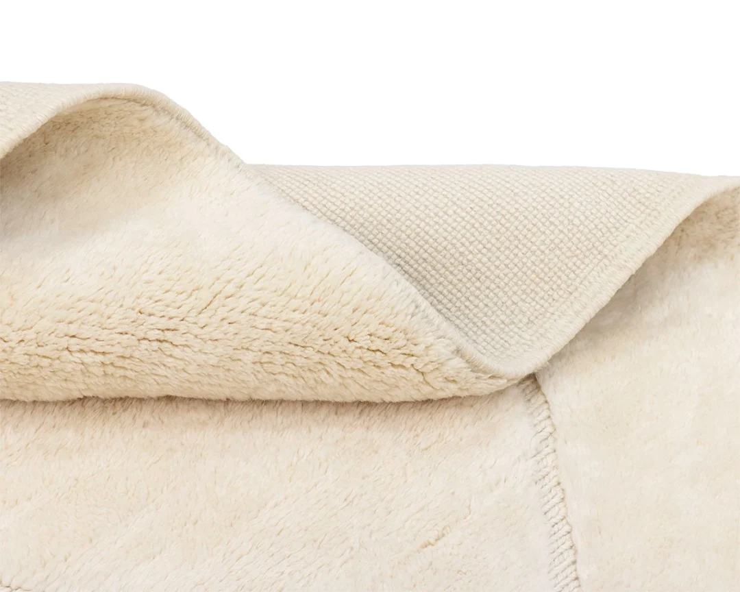 A close-up of a cream-colored fleece blanket, showing its soft, plush surface and the textured underside with a folded corner.