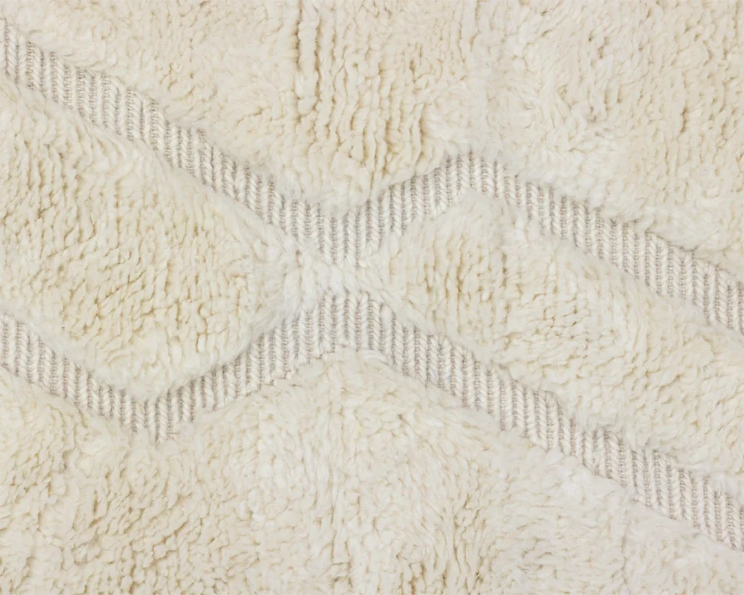 Close-up of a cream-colored, textured fabric with a raised diamond pattern and soft, fluffy fibers.